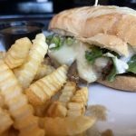 A Steak Sandwich With Melted Cheese, Lettuce, And Cilantro On A Baguette, Served With A Side Of Crinkle Cut Fries And A Small Container Of Sauce., Bevy's Tavern, West des Moines, French dip Sandwich