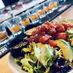 A Vibrant Poke Bowl With Tuna, Avocado, And Mixed Greens, Served Beside A Row Of Sake Glasses In A Bar Setting., Bevy's Tavern, West Des Moines,tuna poke bowl